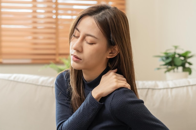 Body muscles stiff problem asian young attractive woman girl pain with back pain ache from work holding massaging rubbing shoulder hurt or sore painful sitting on sofa at home Healthcare people