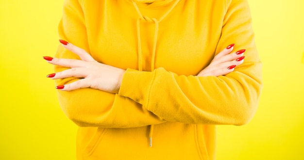 Body part of young woman with arms crossed on yellow background Crop unrecognizable person in yellow hoodie crossed hands with red manicure