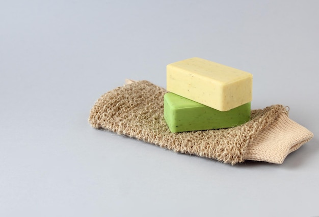 Body washcloth of natural fibers and two natural soaps on blue surface