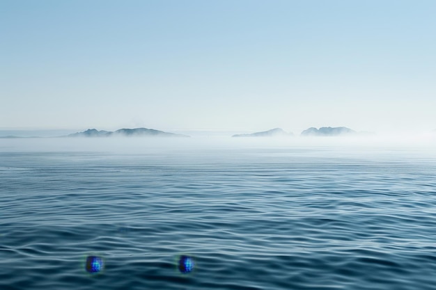 A body of water with a few small islands in the distance on a misty morning A misty morning on the open ocean with fog enveloping distant islands on the horizon