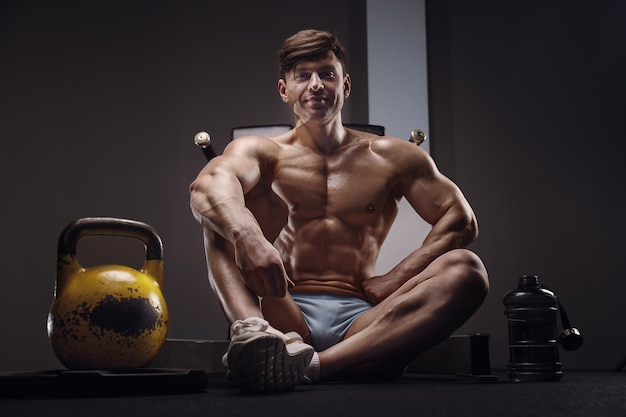 Bodybuilder handsome strong athletic man next to a kettlebell. Workout fitness and bodybuilding healthy concept background