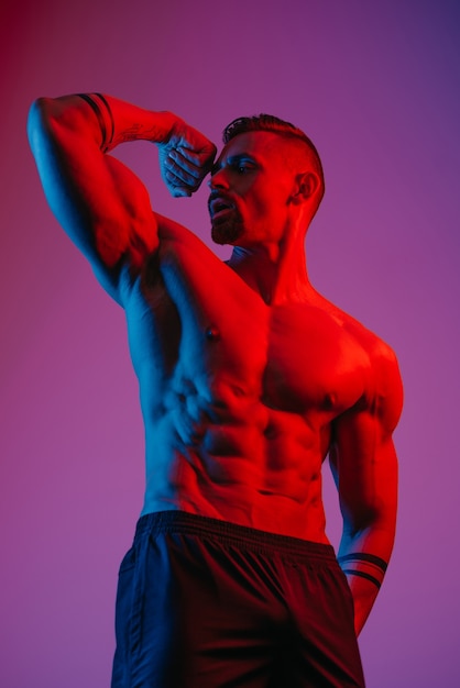 A bodybuilder with a beard is posing with a flexed bicep under the blue and red light