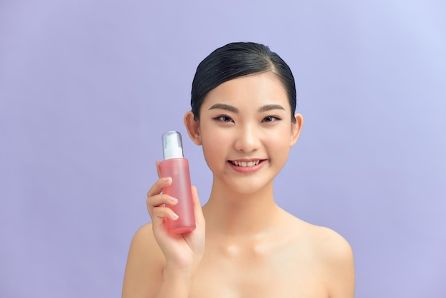 Bodycare and skincare concept Smiling adult asian woman showing dispenser bottle with shower gel soap or body care oil on purple background