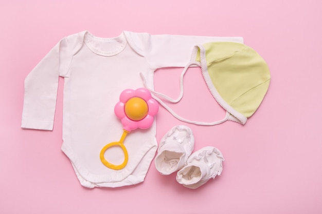 Bodysuit green cap rattle and white booties for a newborn on a pink background