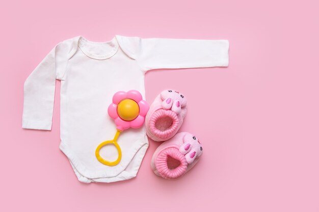 Bodysuit for a newborn rattle and booties on a pink background with copyspace