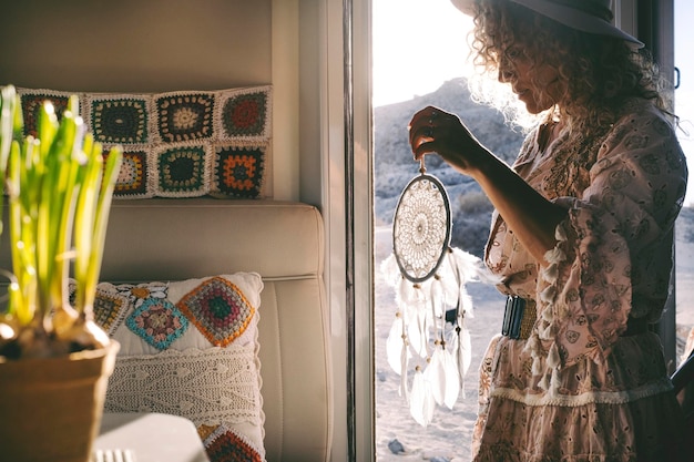 Boho dress style trendy woman on the camper van door with a hand made dreamcatcher Alternative female people enjoying travel wanderlust lifestyle and summer holiday vacation alone inside rv vehicle