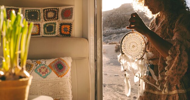 Boho woman traveler standing on the door of her alternative home camper van holding a dreamcatcer Daydreaming lifestyle concept with free female people with scenic background place