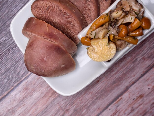 Boiled beef pork tongue with champignon mushrooms studio shot isolated on wood background