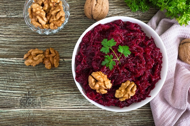 Boiled beetroot with nuts in a white bowl on a wooden background Top view