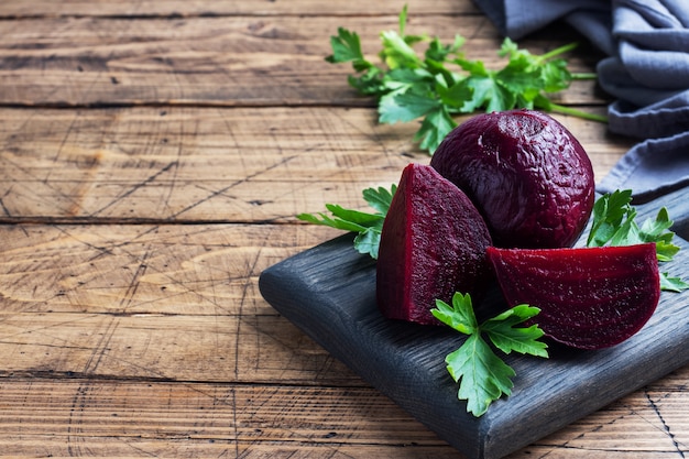 Photo boiled beets whole and cut on a cutting board with parsley leaves on a wooden rustic background.