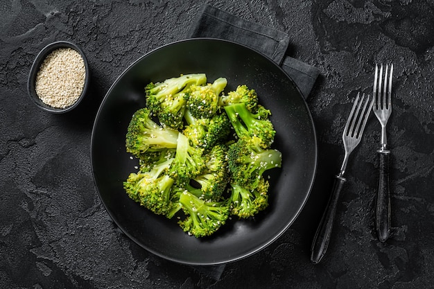 Boiled broccoli with spices in a plate. Black background. Top view.