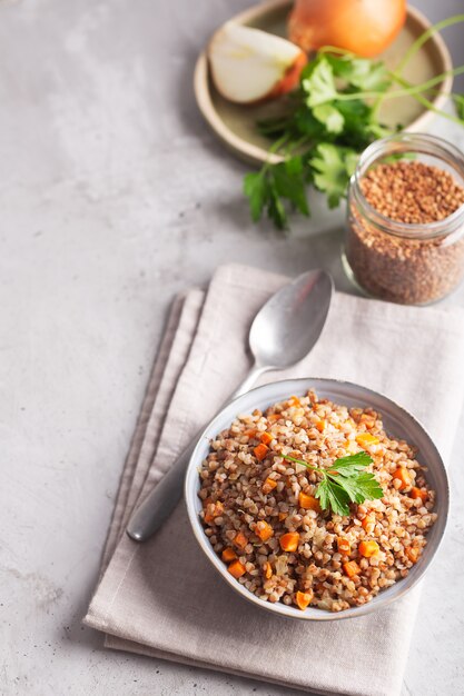 Boiled buckwheat cereal with carrot, parsley and butter in a bowl on a gray background. Traditional Russian dish on gray background with copy space