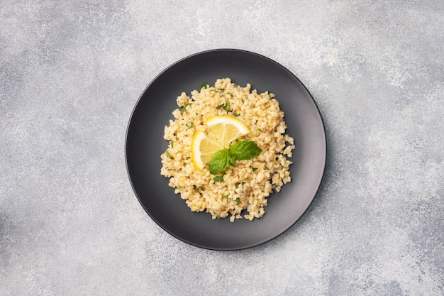 Boiled bulgur with fresh lemon and mint on a plate. A traditional oriental dish called Tabouleh. Gray concrete background top view, copy space