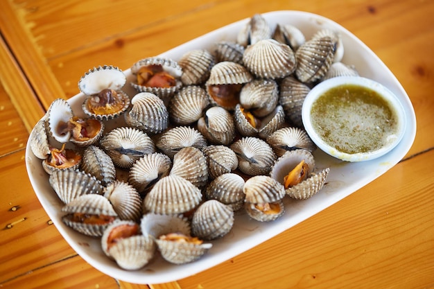 Boiled cockles and spicy and sour seafood sauce served on a white plate and placed on a wooden table seafood popular in Thailand local food