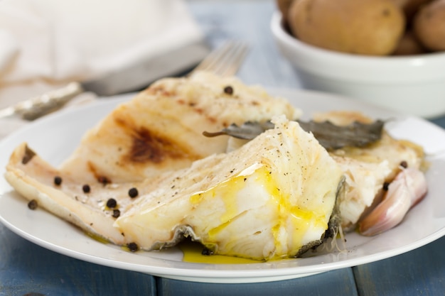 Boiled codfish on white plate and boiled potato in bowl