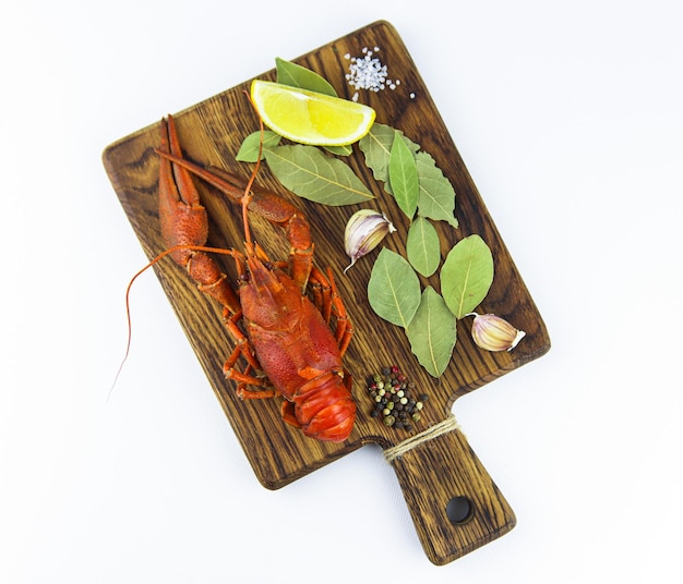 Boiled crayfish with lemon, herbs and garlic on a wooden cutting board on white background.