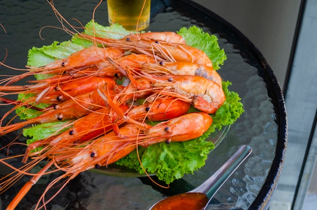 Boiled delicious king shrimp on green lettuce leaves with Thai sweet and sour sauce on a glass table