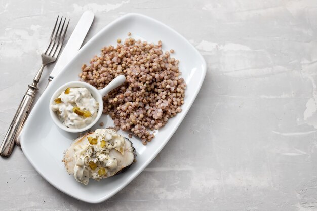 Boiled fish with buckwheat and sauce on white dish on ceramic table