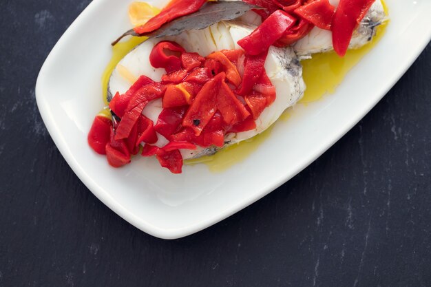 Boiled fish with red pepper and olive oil on white dish