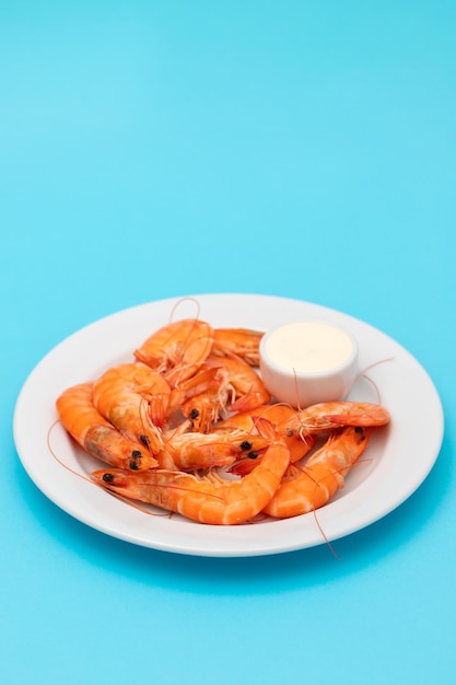 Boiled fresh shrimps with sauce in small bowl on white plate on blue