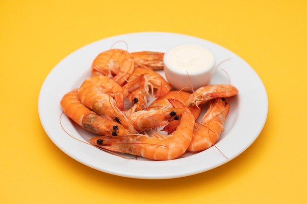 Boiled fresh shrimps with sauce in small bowl on white plate on yellow