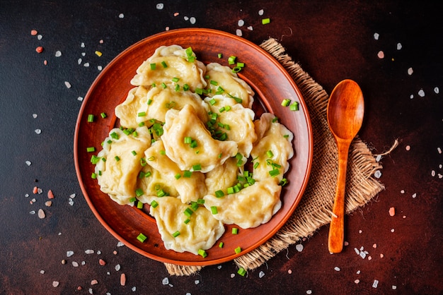 The boiled made dumplings with a stuffing with oil and green onions on a dark table. It can be used as a background