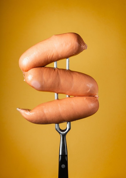 Boiled milk sausages on a fork on a yellow background The concept of fast food hearty food