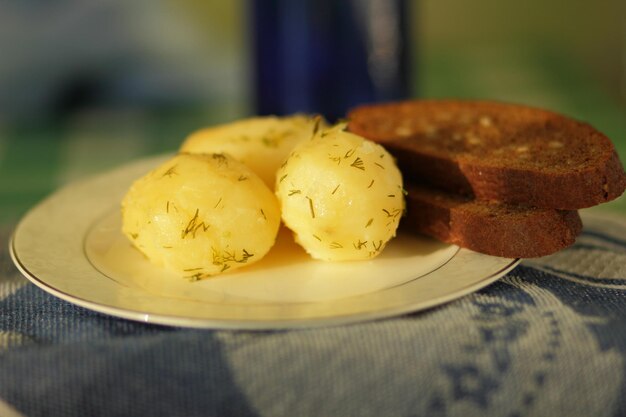 Boiled new potatoes with dill and black bread on a white plate with a blue napkin Closeup of tasty healthy food in home kitchen Vegetarian food concept