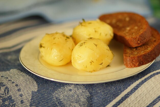 Boiled new potatoes with dill and black bread on a white plate with a blue napkin Closeup of tasty healthy food in home kitchen Vegetarian food concept