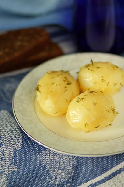 Boiled new potatoes with dill and black bread on a white plate with a blue napkin Closeup of tasty healthy food in home kitchen Vegetarian food concept