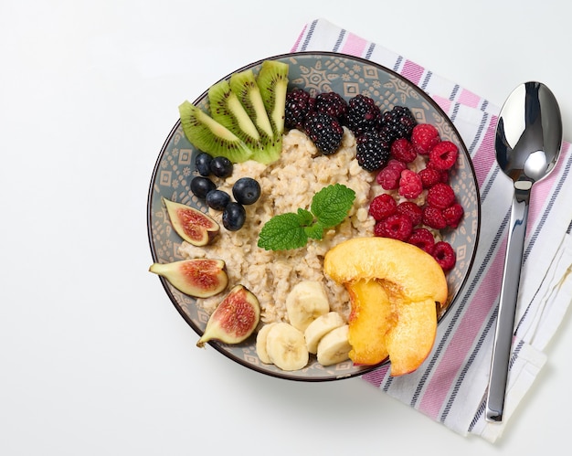 Boiled oatmeal with fruit in a round plate on a white table, healthy breakfast. View from above