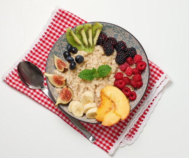 Boiled oatmeal with fruit in a round plate on a white table, healthy breakfast. View from above