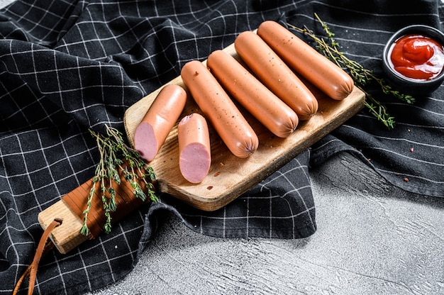 Boiled pork classic sausages on a cutting Board with rosemary and spices. Black background. Top view