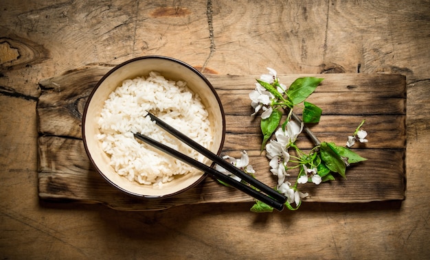 Boiled rice in a bowl and Sakura. On a wooden table.