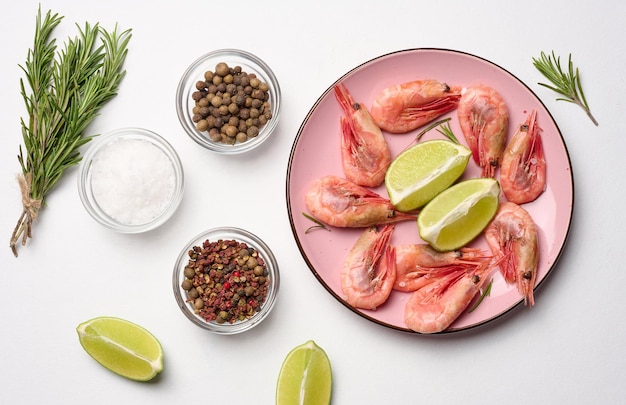 Boiled shrimp lemon and lime slices spices in a round pink plate on a white background top view