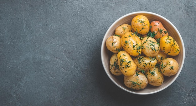 Boiled unpeeled potatoes with dill and butter on a dark background