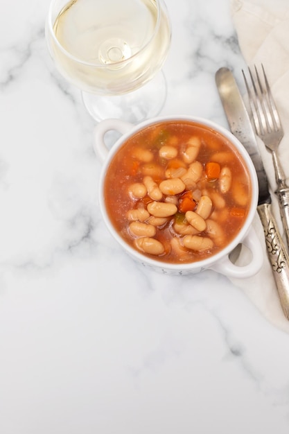 Boiled white beans with vegetables and sauce on white bowl