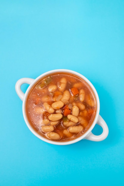 Boiled white beans with vegetables and sauce on white bowl