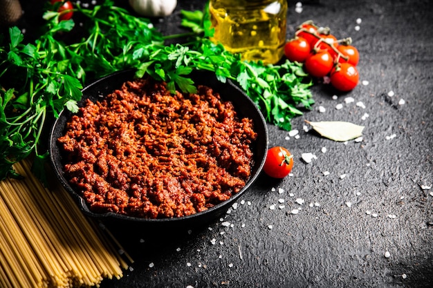 Bolognese sauce in a frying pan with pasta dry and parsley