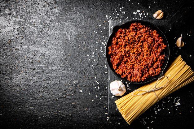 Bolognese sauce on a stone board with a bunch of dry pasta and garlic