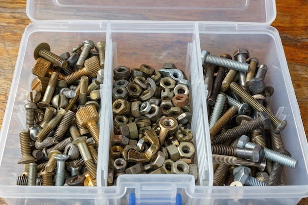 Bolts and nuts of different sizes in opened storage box on wooden table in workshop