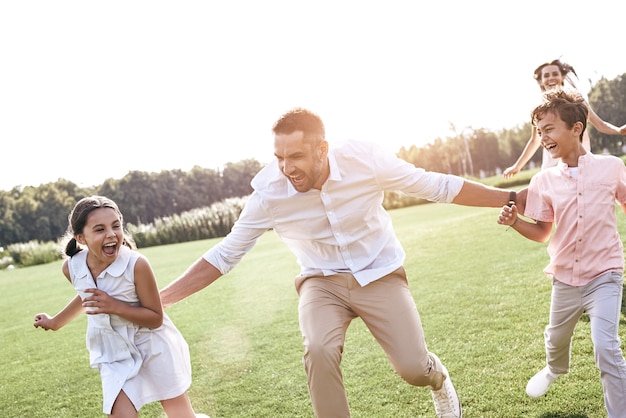 Bonding family of four running on grassy field playing playing