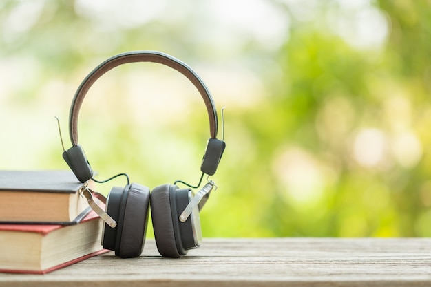 Book and black headphone on wooden table with abstract green nature blur. Reading and education concept