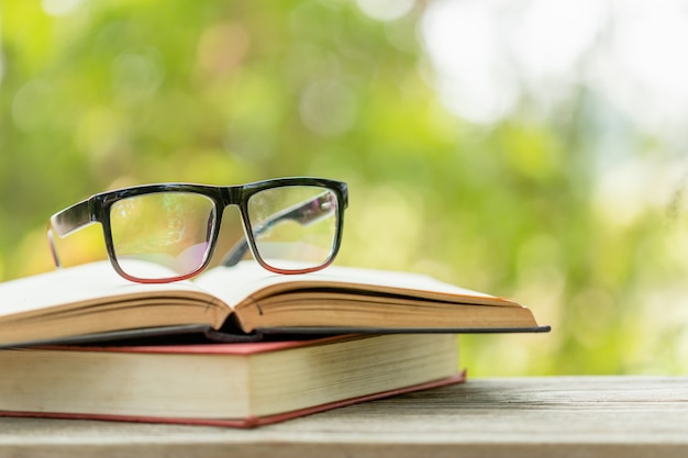 Book and eye glasses on wooden table with abstract green nature blur  Reading and education concept