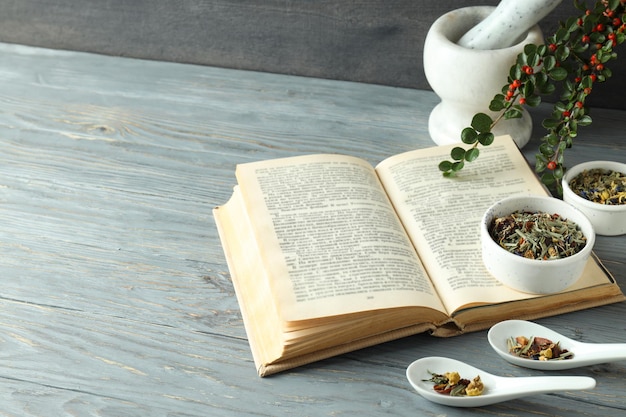 Book and herbs in scoops and bowls on wooden background space for text