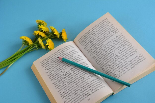 book with green pencil and bunch of yellow dandelions, close-up