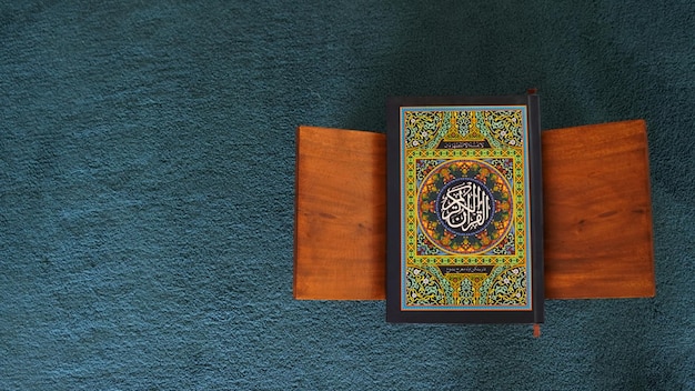 A book with the name of allah on it sits on a blue carpet.