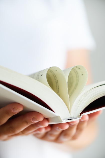 Book with opened pages and shape of heart in girl hands. 