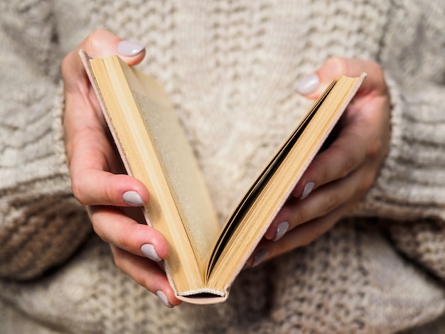 Book in women's hands. A girl in a wool sweater is holding a book. Cozy atmosphere.