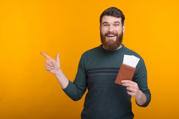 Book your trip here. Young man is pointing aside while holding passport and tickets.